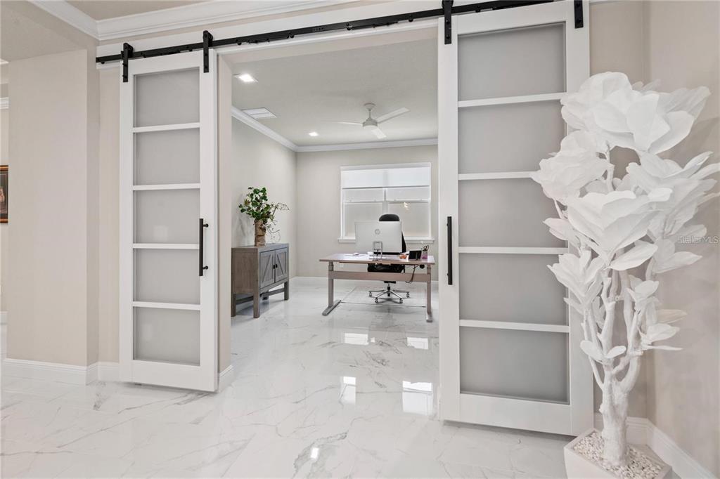 A home office with white marble floors is visible through open frosted glass barn doors — 5697 LONG SHORE LOOP, SARASOTA, FL