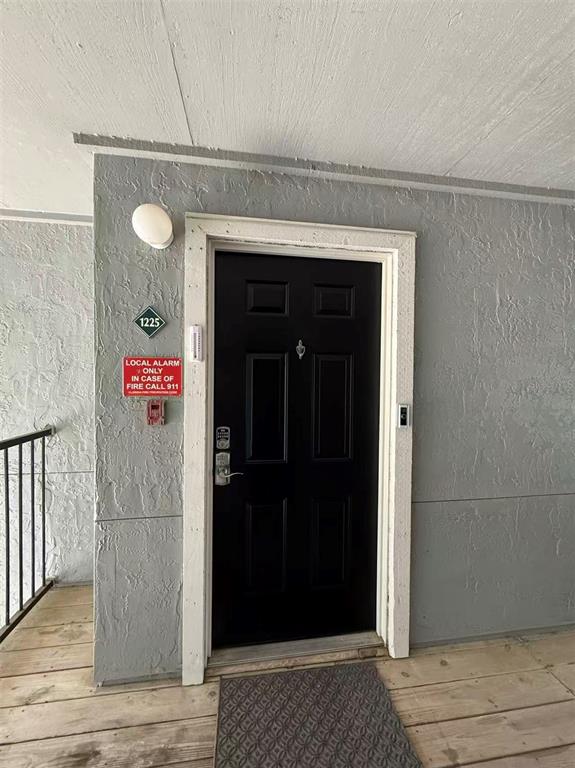 A black front door with a fire alarm sign is set in a gray stucco wall — 3705 SW 27TH STREET UNIT 1225, GAINESVILLE, FL