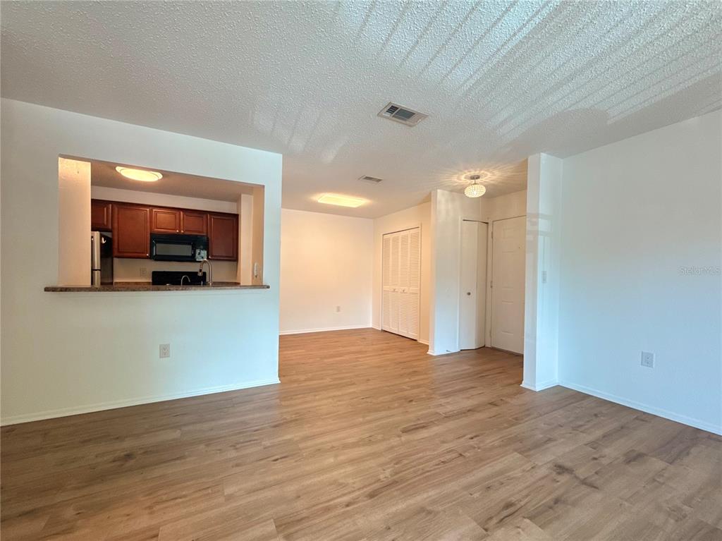 An open-concept living area features wood-look flooring and a pass-through window to the kitchen — 3705 SW 27TH STREET UNIT 1225, GAINESVILLE, FL