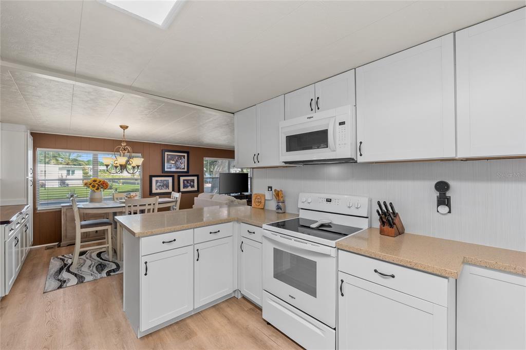 A kitchen with white cabinets, light countertops, and a white stove, opening to a dining area — 288 SALEM AVENUE UNIT 3, PALM HARBOR, FL