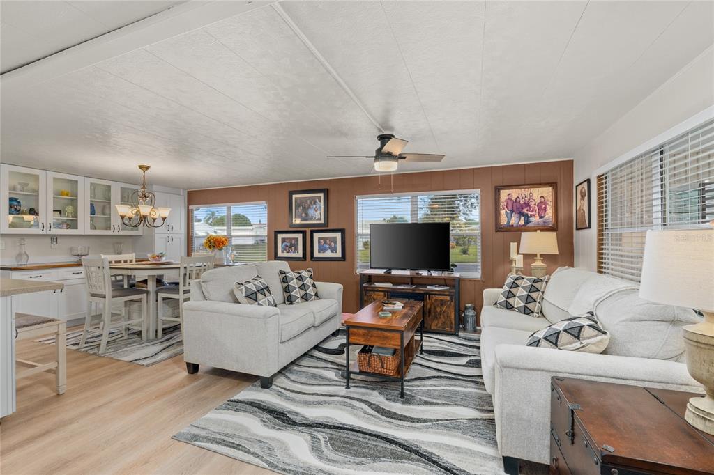A living room and dining area feature light wood floors, white sofas, and brown walls — 288 SALEM AVENUE UNIT 3, PALM HARBOR, FL
