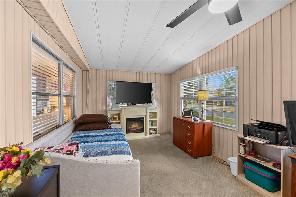 A sunroom features a daybed, a fireplace with a television above it, and carpeted flooring — 288 SALEM AVENUE UNIT 3, PALM HARBOR, FL