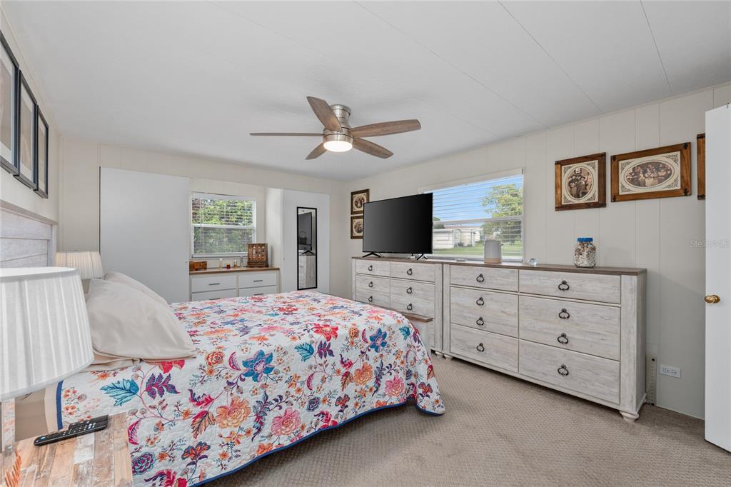 A bedroom features a floral bedspread, a large dresser with a television, and a ceiling fan — 288 SALEM AVENUE UNIT 3, PALM HARBOR, FL