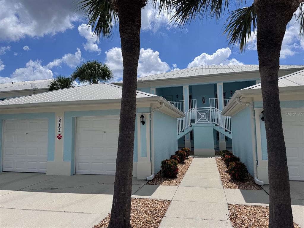 A light blue two-story building features white garage doors, a central staircase, and palm trees — 5764 SABAL TRACE DRIVE UNIT 201, NORTH PORT, FL