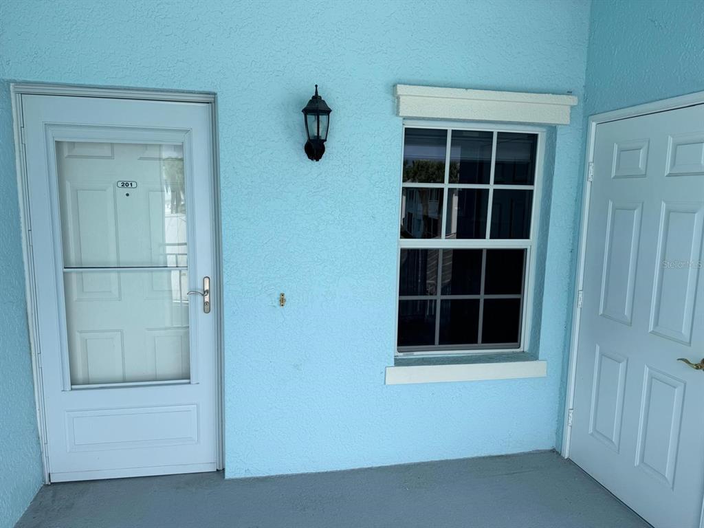 A light blue exterior wall features a white storm door, a window, and a light fixture — 5764 SABAL TRACE DRIVE UNIT 201, NORTH PORT, FL