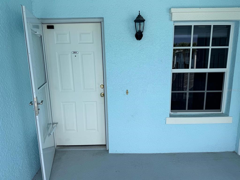 A white front door labeled 201 sits next to a window on a light blue wall — 5764 SABAL TRACE DRIVE UNIT 201, NORTH PORT, FL