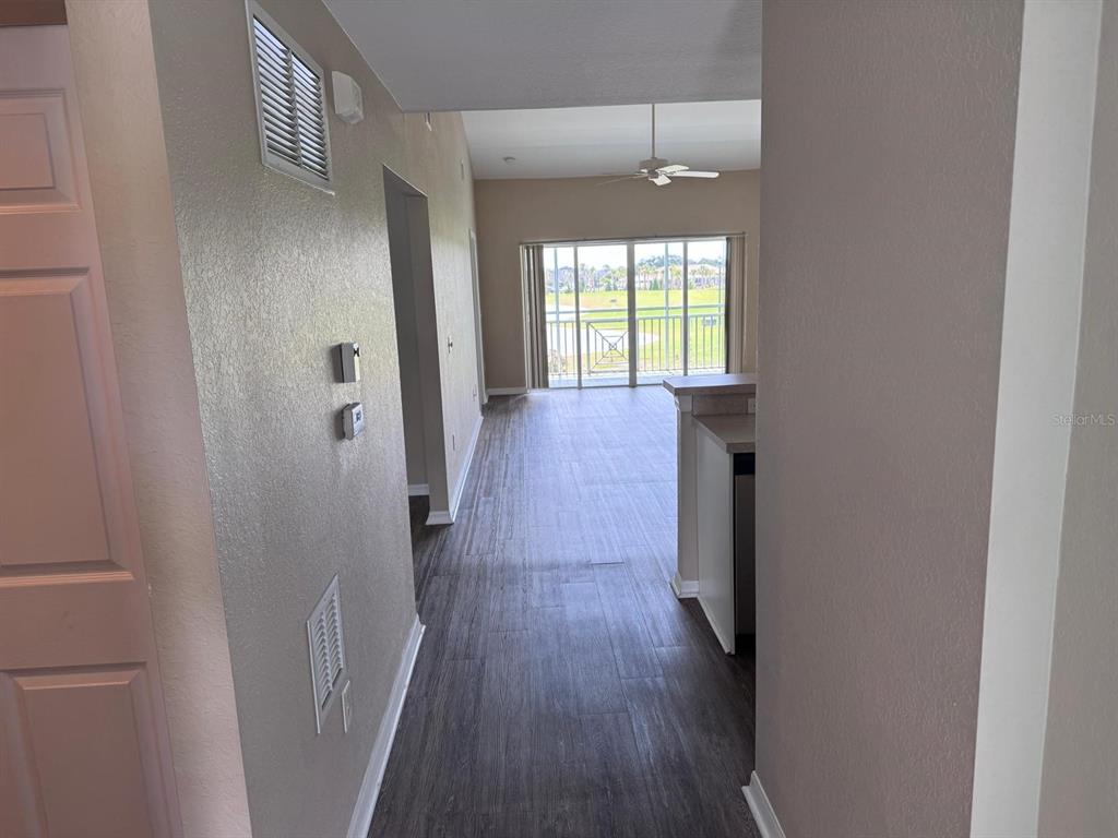 A hallway with wood-look flooring leads to an open living area with a balcony view — 5764 SABAL TRACE DRIVE UNIT 201, NORTH PORT, FL