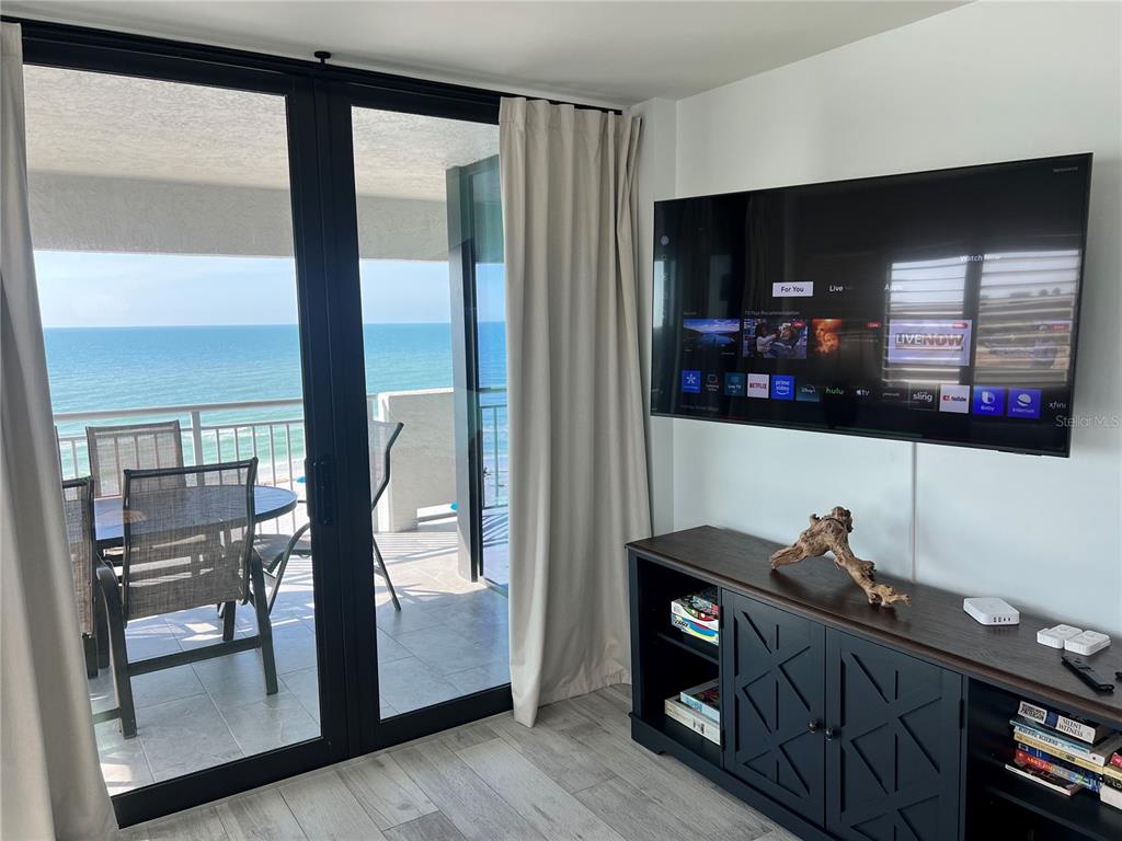 A living room features a wall-mounted television, a dark media console, and a balcony overlooking the ocean — 1001 POINT OF ROCKS ROAD UNIT 611, SARASOTA, FL