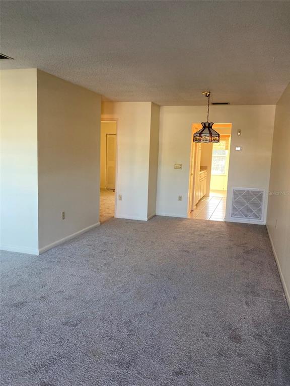 A carpeted living room leads to a dining area with a hanging stained-glass light fixture — 5750 80TH STREET N UNIT C202, ST PETERSBURG, FL
