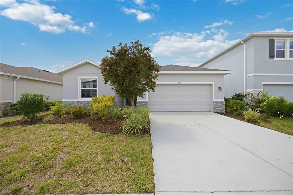 A single-story house with a light gray exterior, a two-car garage, and a concrete driveway — 5719 WOODLAND SAGE DRIVE, SARASOTA, FL