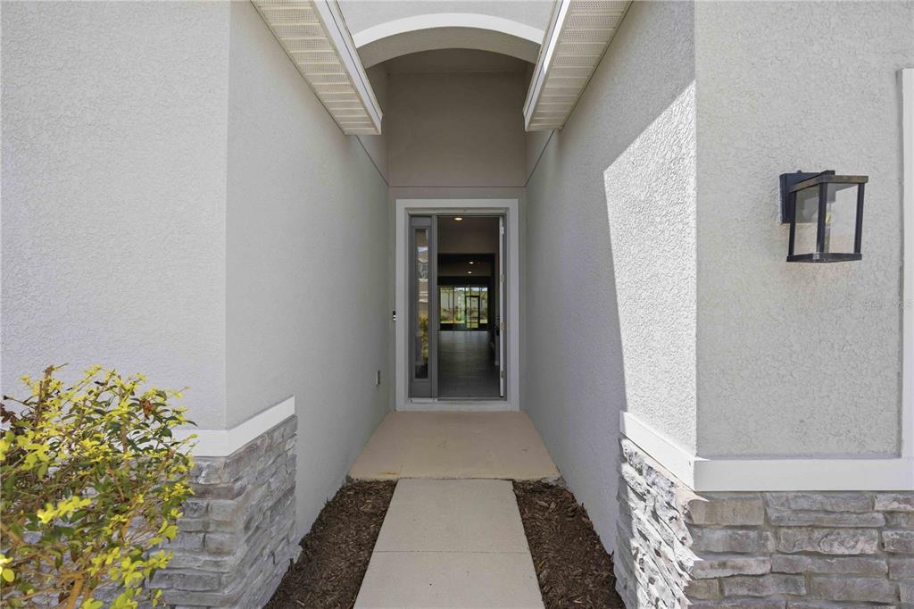 A concrete walkway leads to the front entrance of a house with stone veneer accents — 5719 WOODLAND SAGE DRIVE, SARASOTA, FL