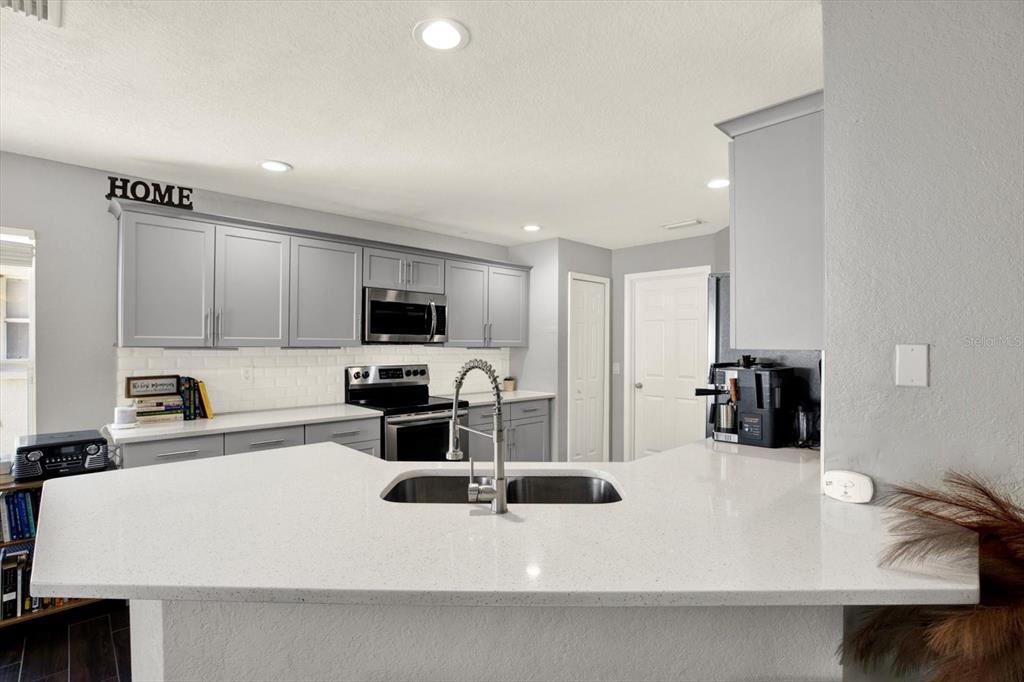 A kitchen features gray cabinets, white countertops, a subway tile backsplash, and a peninsula sink — 11434 CRESTLAKE VILLAGE DRIVE, RIVERVIEW, FL