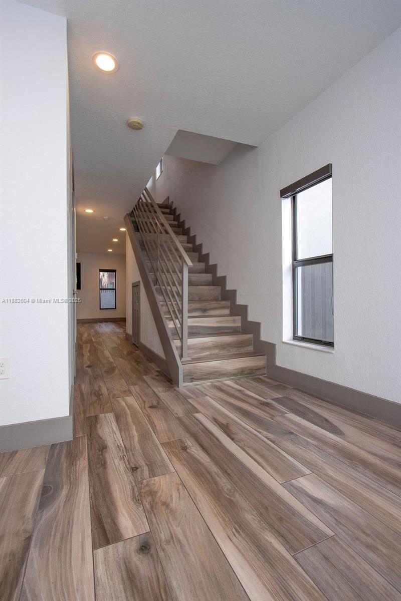 A staircase with wood-look flooring and a metal railing sits in a modern hallway — 2061 Washington Ave # 4, Opa-Locka FL 33054, OPA-LOCKA, FL