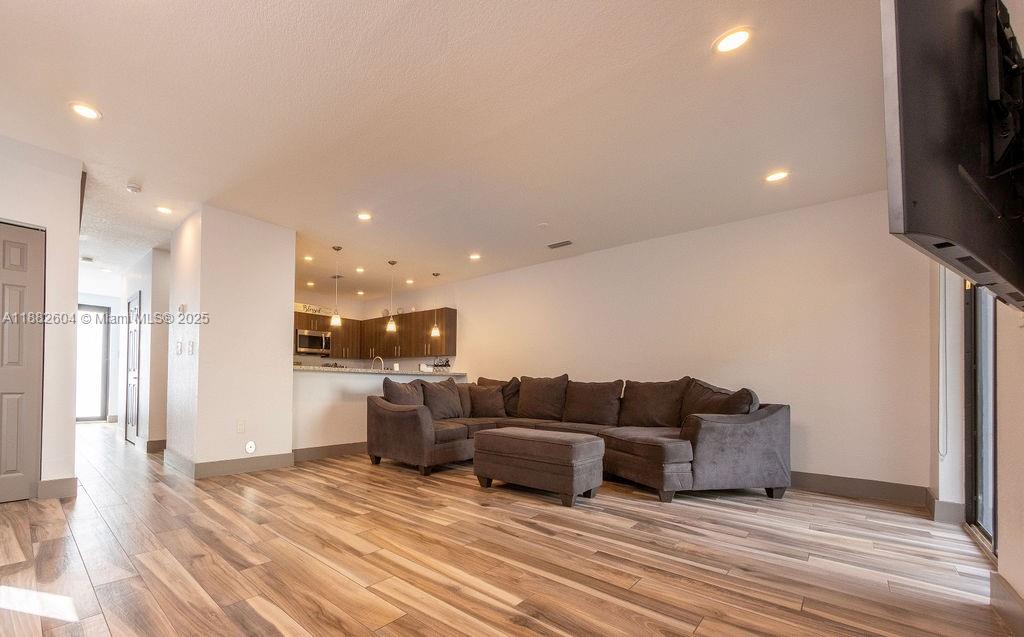 A living room with wood-look flooring features a large gray sectional sofa and kitchen — 2061 Washington Ave # 4, Opa-Locka FL 33054, OPA-LOCKA, FL