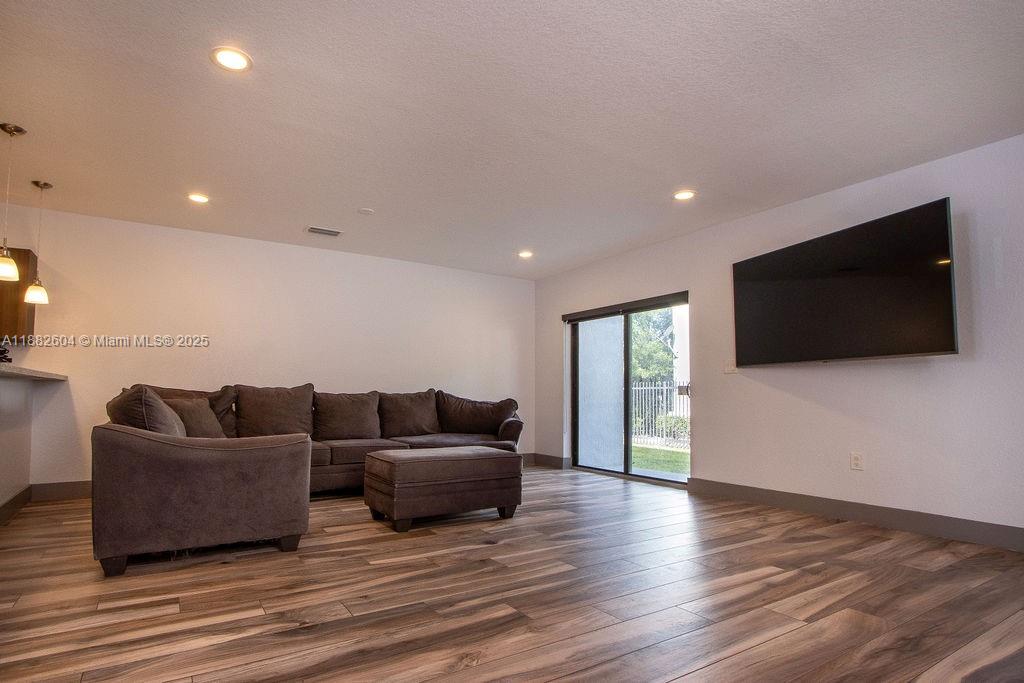 A living room features a dark sectional sofa, wood-look flooring, and a wall-mounted television — 2061 Washington Ave # 4, Opa-Locka FL 33054, OPA-LOCKA, FL