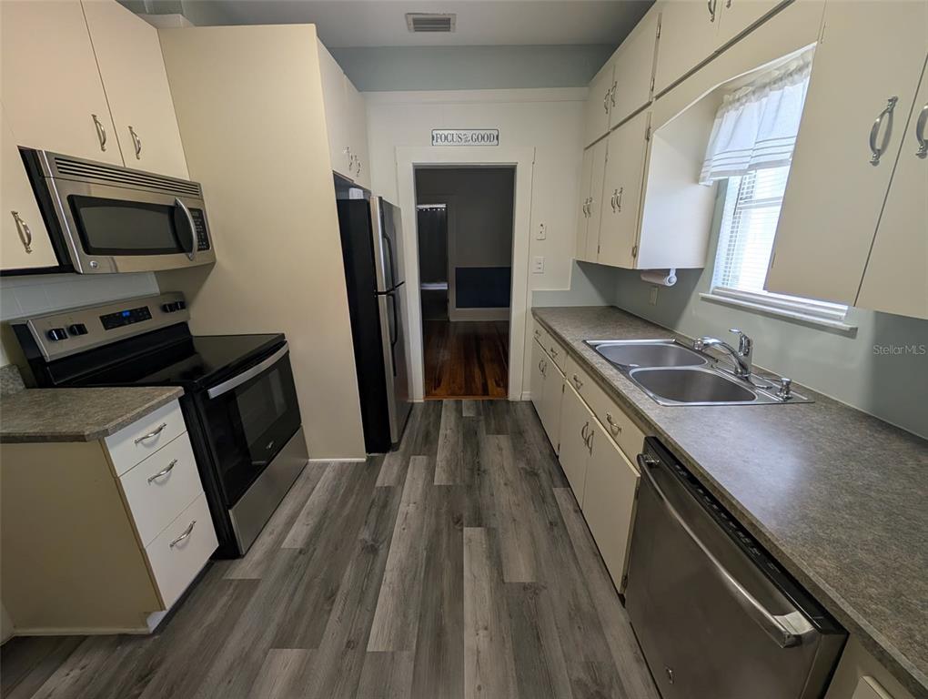 A kitchen features light-colored cabinets, stainless steel appliances, a double sink, and wood-look flooring — 321-B W PENNSYLVANIA AVENUE, DELAND, FL