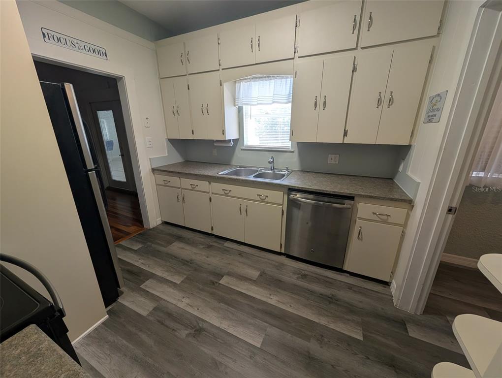A kitchen features white cabinets, a stainless steel dishwasher, a sink, and wood-look flooring — 321-B W PENNSYLVANIA AVENUE, DELAND, FL