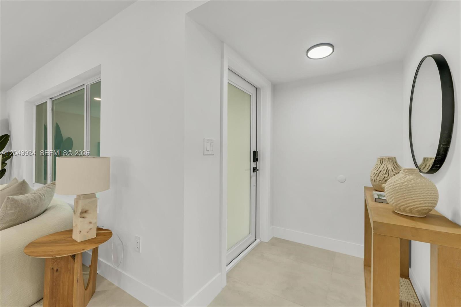 A bright entryway features white walls, tile flooring, a glass door, and minimalist wooden furniture — 8970 SW 53rd St, Cooper City FL 33328, COOPER CITY, FL