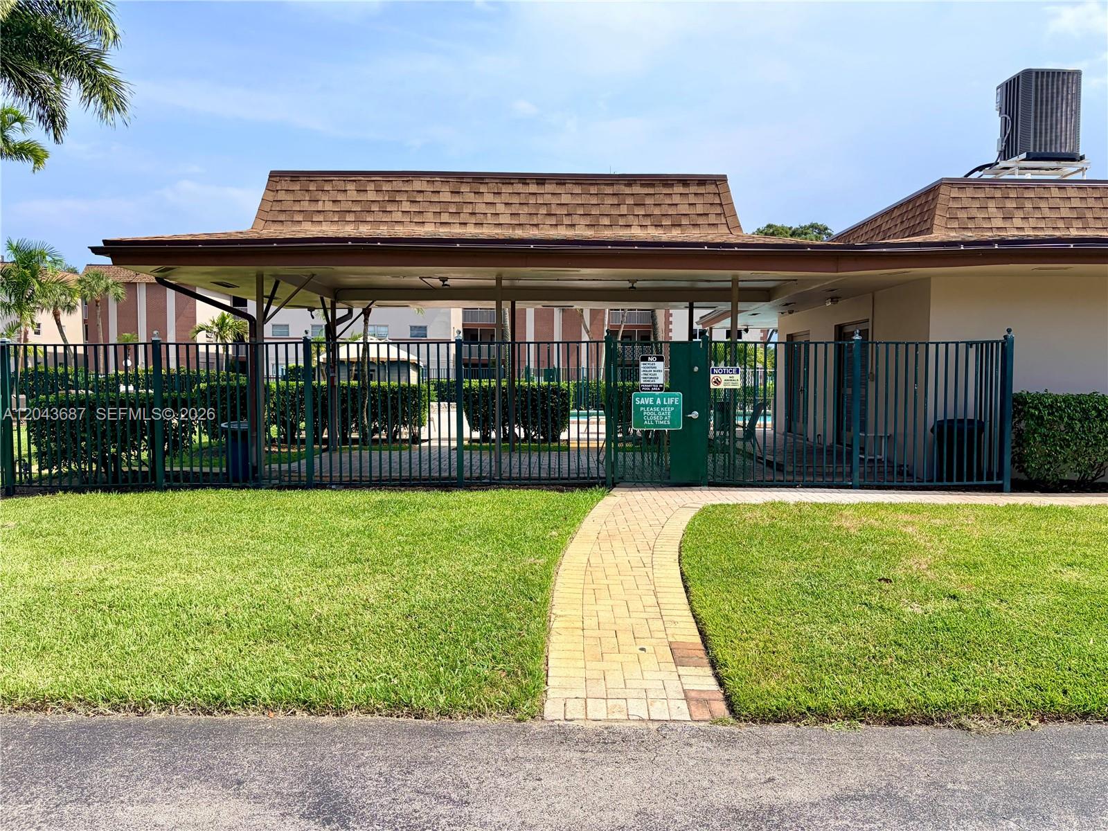 A paved walkway leads to a gated entrance of a community pool area with a roof — 8101 SW 24th Ct # 405, Davie FL 33324, DAVIE, FL