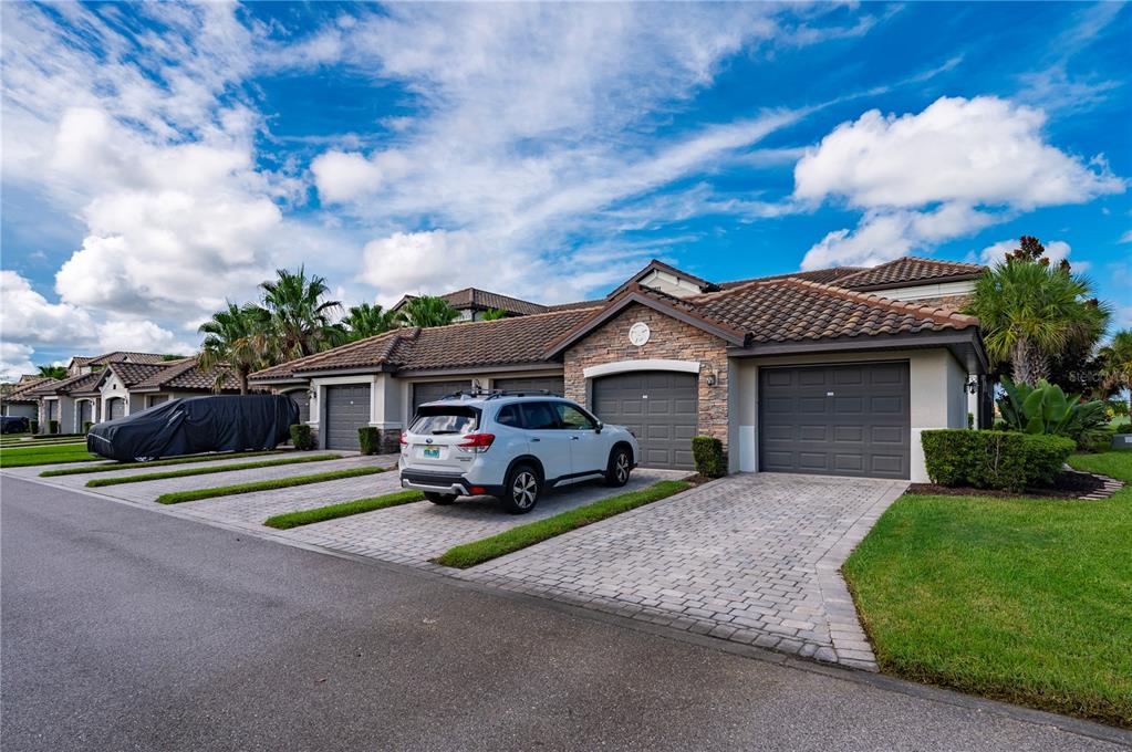 A row of attached houses with tiled roofs, stone accents, and paved driveways under a sky — 5517 PALMER CIRCLE UNIT 106, BRADENTON, FL
