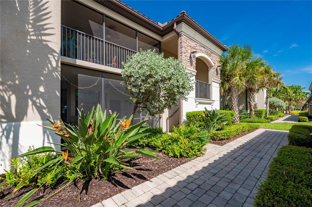 A two-story building with screened balconies, stone accents, and a paved walkway through landscaping — 5517 PALMER CIRCLE UNIT 106, BRADENTON, FL