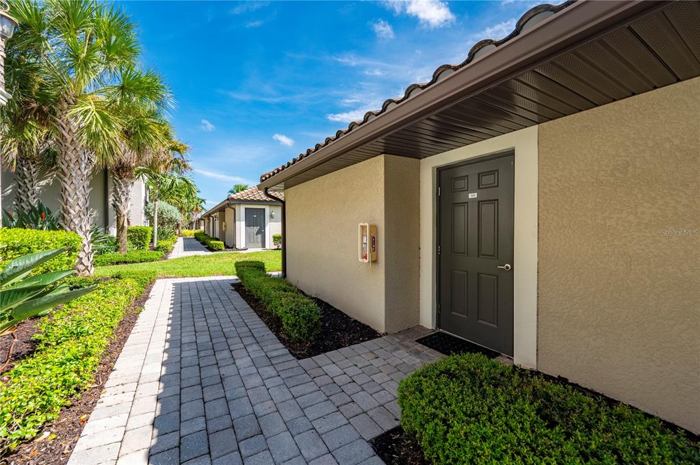 A paved walkway leads to a dark gray door on the side of a building — 5517 PALMER CIRCLE UNIT 106, BRADENTON, FL