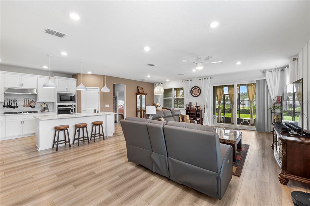 A spacious open-concept kitchen and living room featuring white cabinetry, a breakfast bar, and wood-look flooring — 783 LITTLE CLOUD PLACE, VALRICO, FL