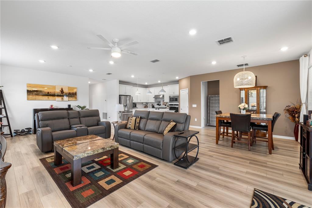 An open-concept living and dining area features gray leather sofas, wood-look flooring, and white cabinetry — 783 LITTLE CLOUD PLACE, VALRICO, FL