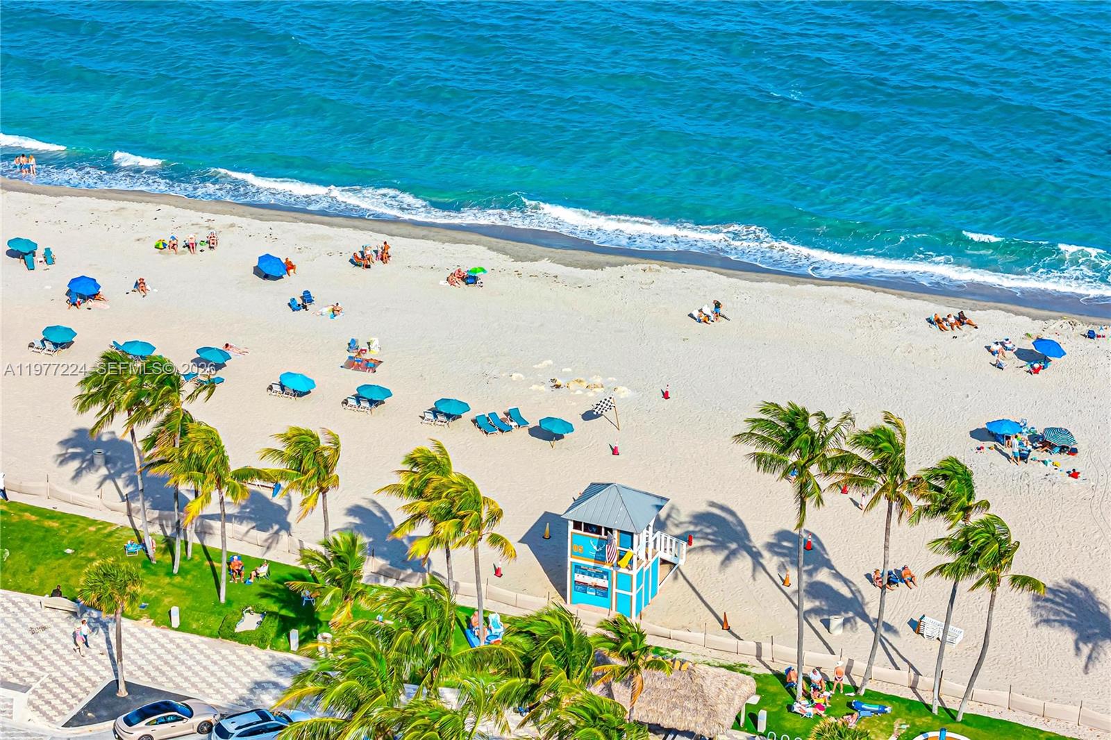 An aerial view shows a sandy beach with palm trees, umbrellas, and a lifeguard station — 2051 SE 3rd St # 407, Deerfield Beach FL 33441, DEERFIELD BEACH, FL
