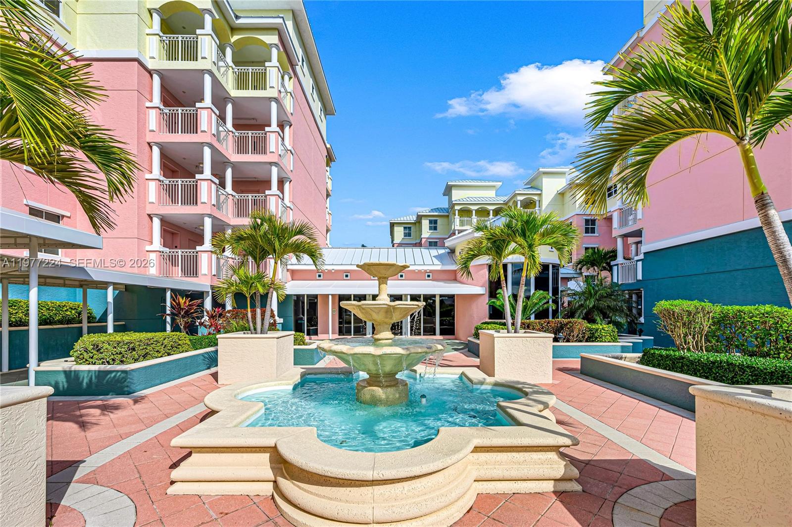 A tiered stone fountain sits in a courtyard between pink multi-story apartment buildings — 2051 SE 3rd St # 407, Deerfield Beach FL 33441, DEERFIELD BEACH, FL