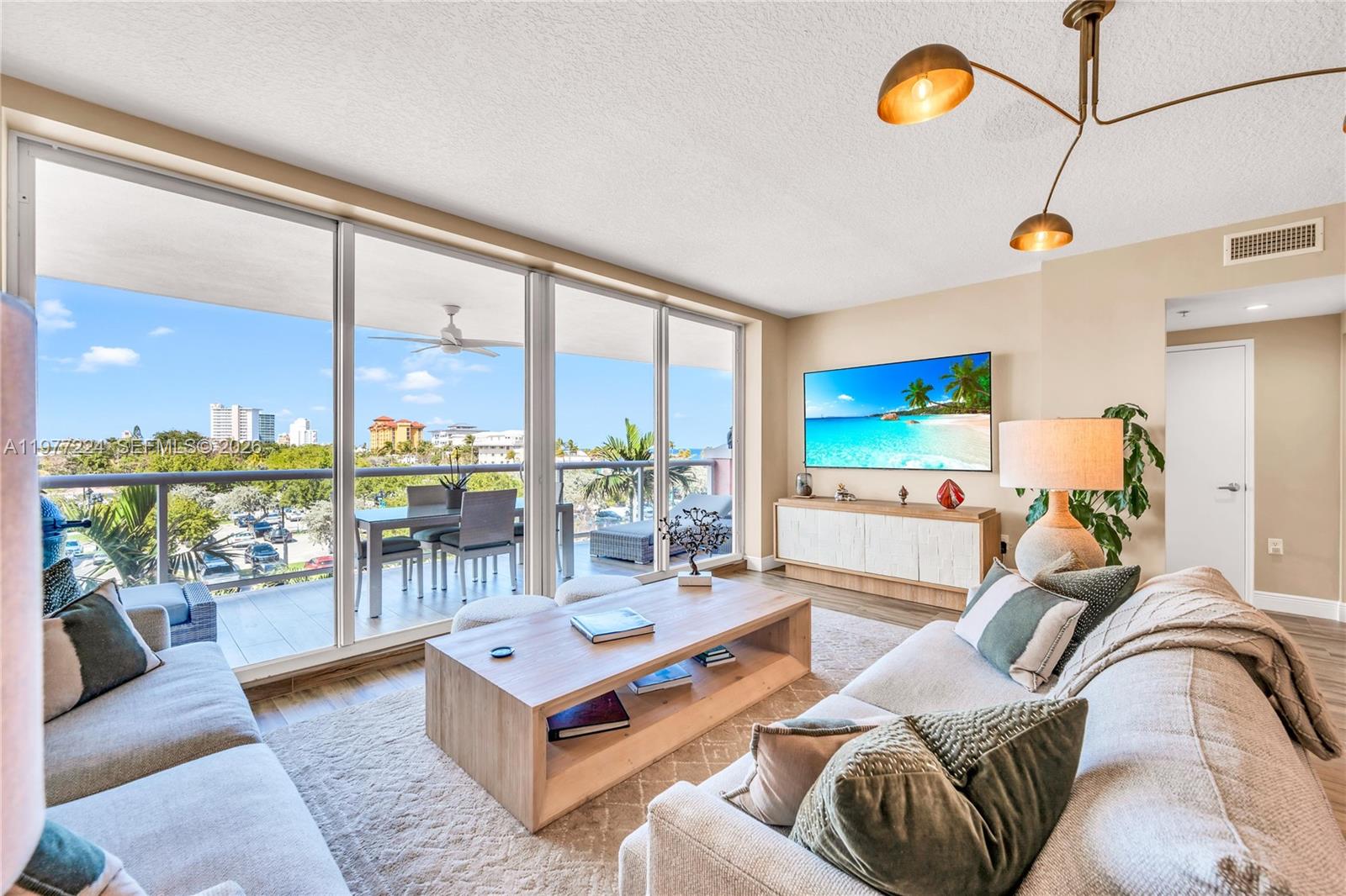 A living room features a large balcony, light wood furniture, and a wall-mounted television — 2051 SE 3rd St # 407, Deerfield Beach FL 33441, DEERFIELD BEACH, FL