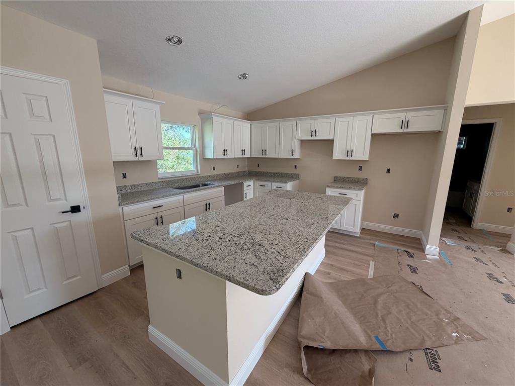 A kitchen with white cabinets, granite countertops, a central island, and light wood-look flooring — 851 SE 28TH STREET, OCALA, FL