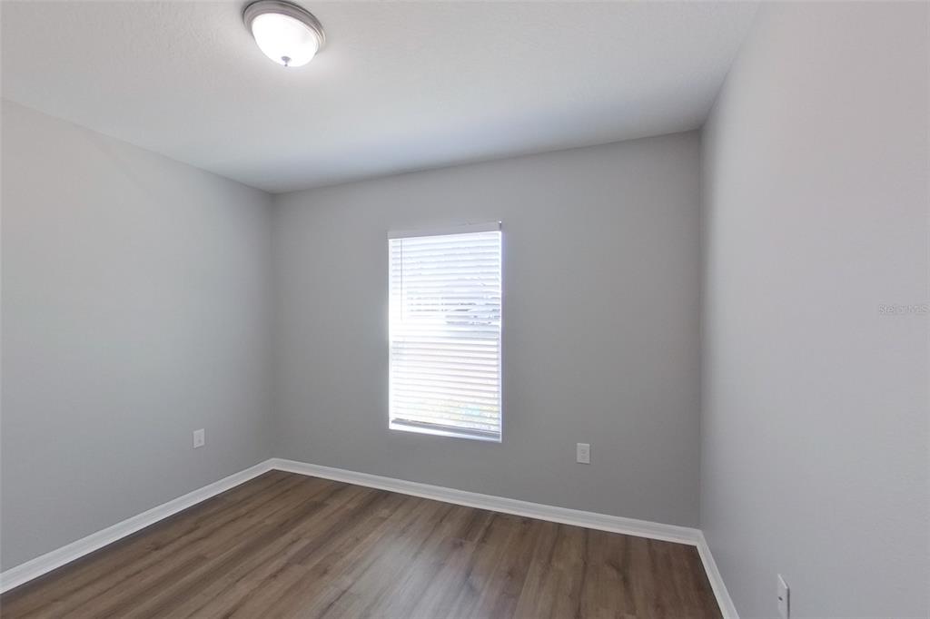 An empty bedroom features light gray walls, wood-look flooring, a single window, and a ceiling light — 9810 N SANTEE TERRACE, DUNNELLON, FL