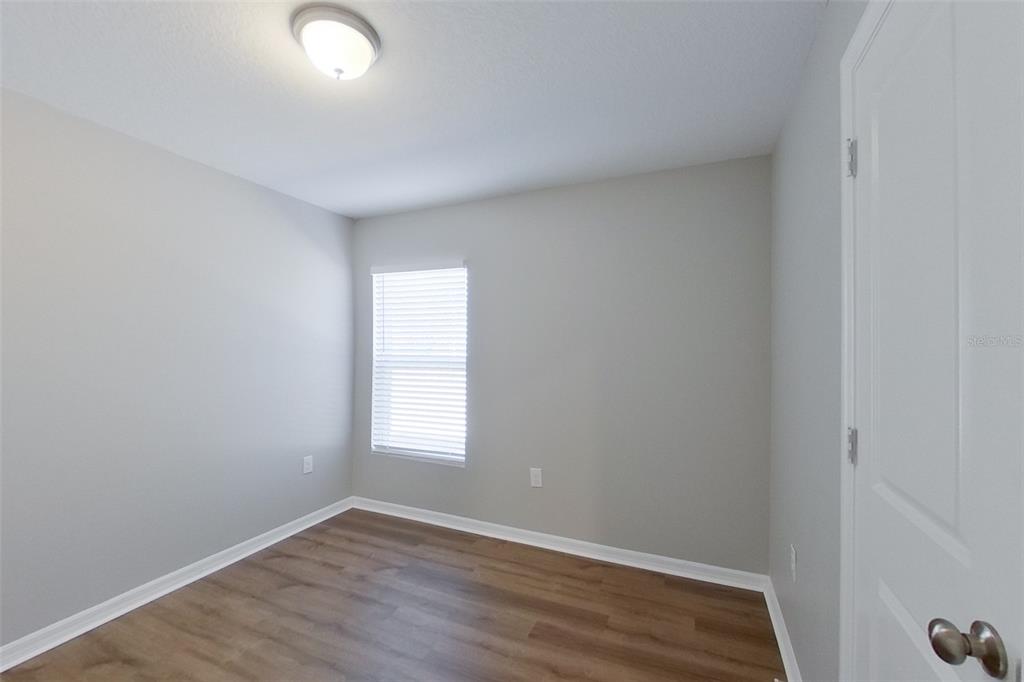 An empty bedroom features light gray walls, wood-look flooring, a window with blinds, and lighting — 9810 N SANTEE TERRACE, DUNNELLON, FL