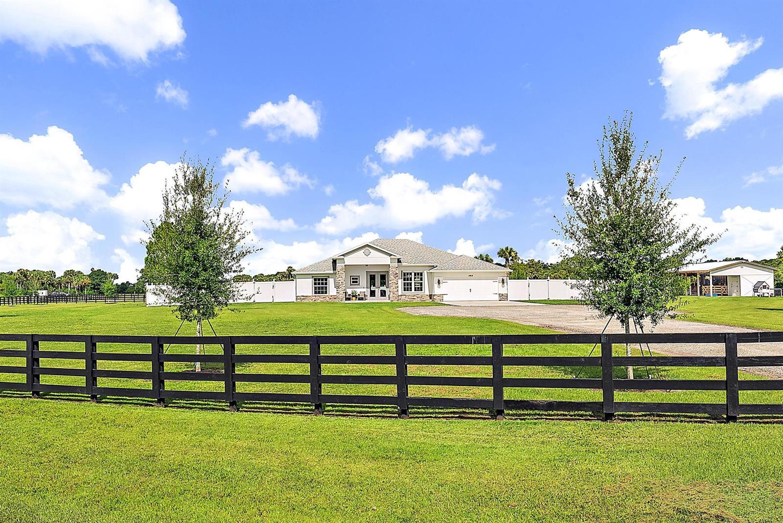 A single-story house with a white exterior and stone accents sits behind a black fence — 13615 SE 26th Lane, Okeechobee FL 34974, OKEECHOBEE, FL
