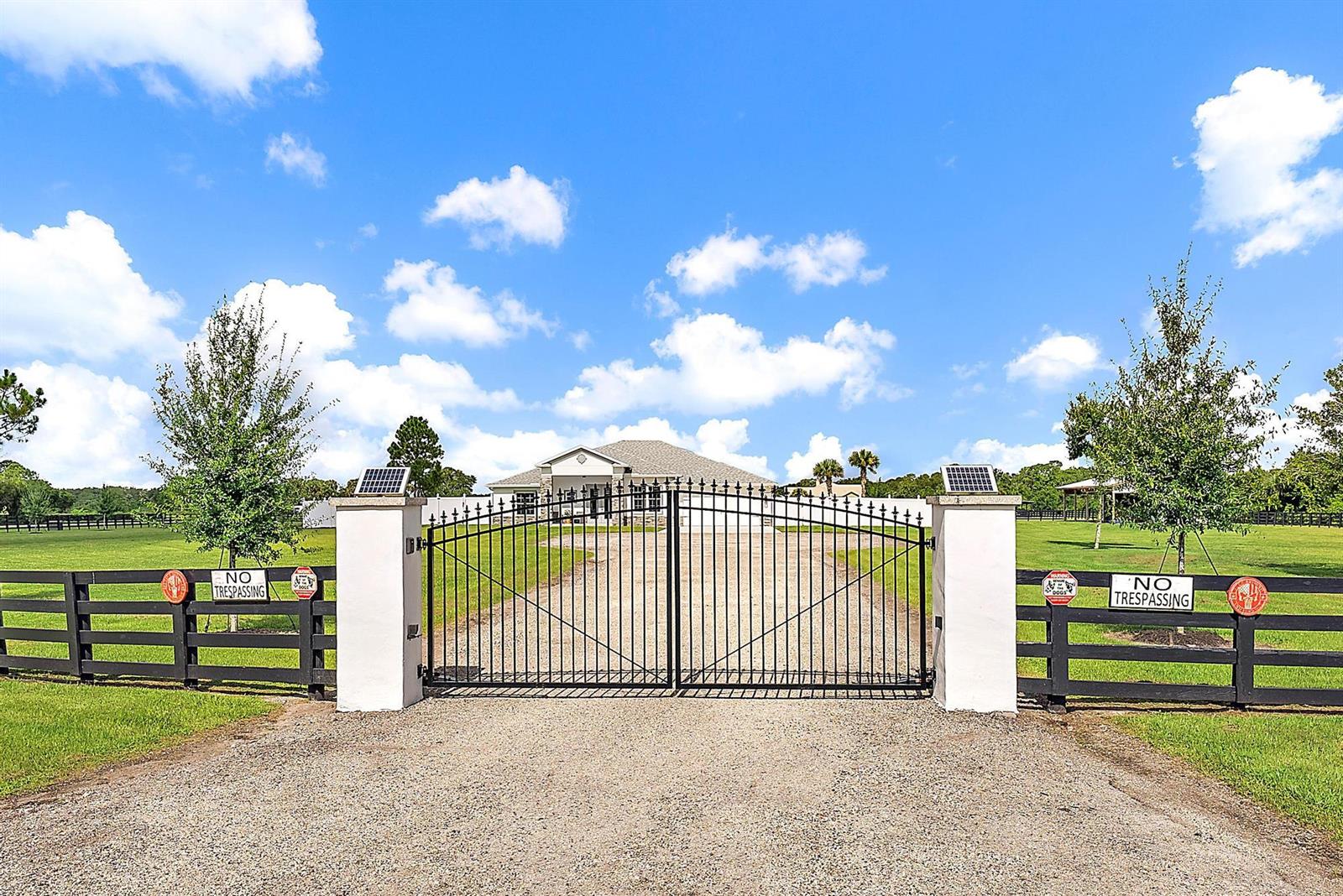 A gravel driveway leads to a gated entrance with white pillars and black fencing — 13615 SE 26th Lane, Okeechobee FL 34974, OKEECHOBEE, FL