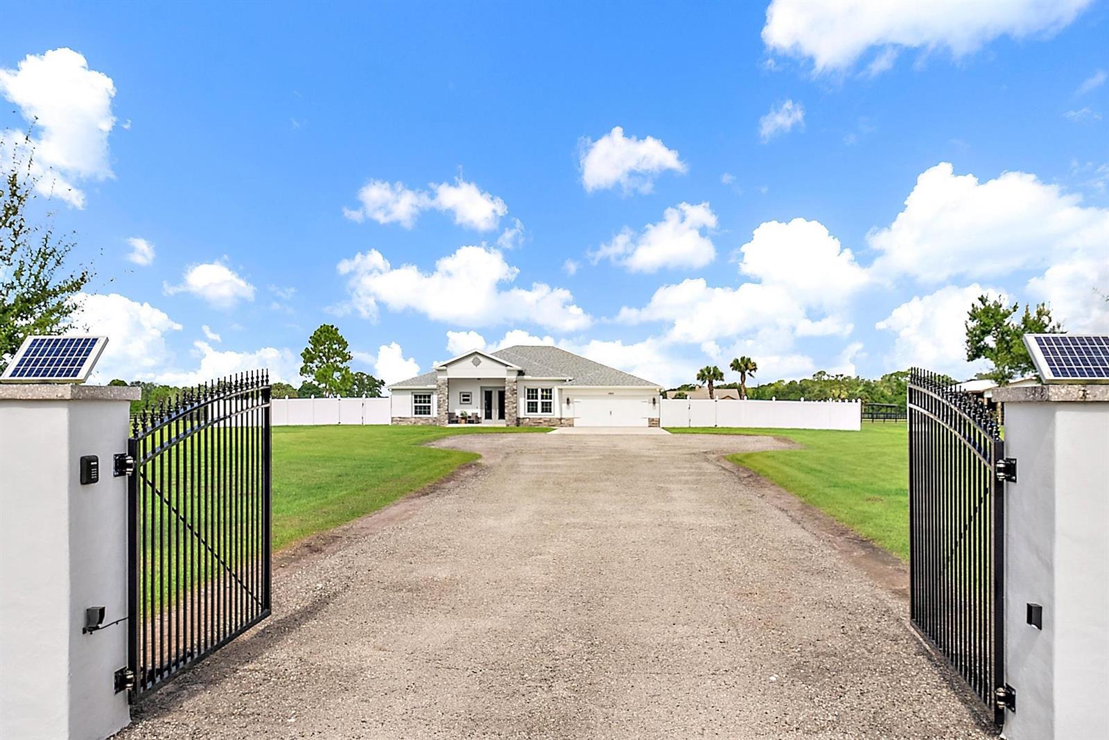 A gravel driveway leads through an open gate toward a single-story house with a garage — 13615 SE 26th Lane, Okeechobee FL 34974, OKEECHOBEE, FL