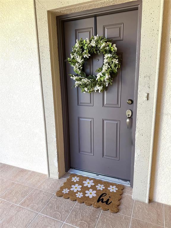 A front door with a floral wreath and a daisy-patterned welcome mat on a porch — 35 RIVERVIEW BEND S UNIT 1845, PALM COAST, FL