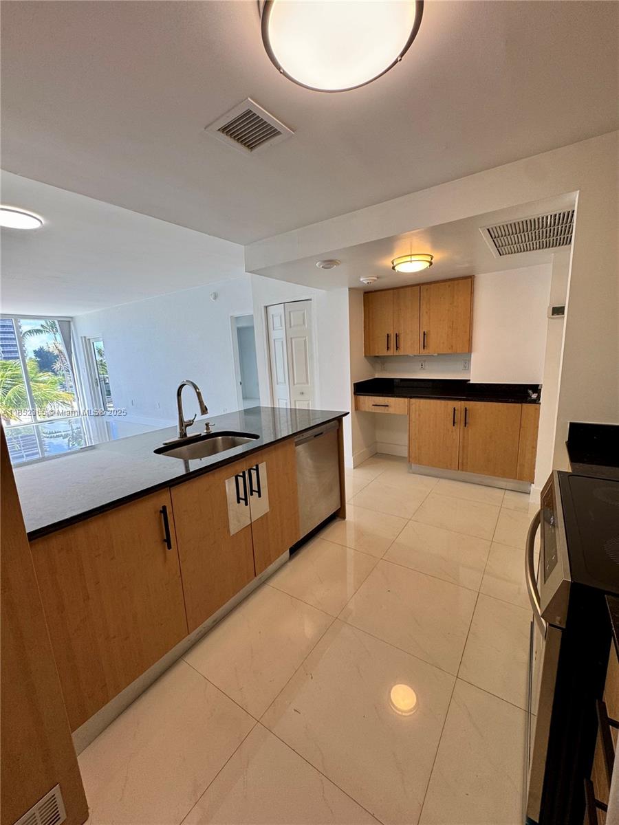 A kitchen features light wood cabinets, black countertops, stainless steel appliances, and white tile flooring — 10275 Collins Ave # 316, Bal Harbour FL 33154, BAL HARBOUR, FL