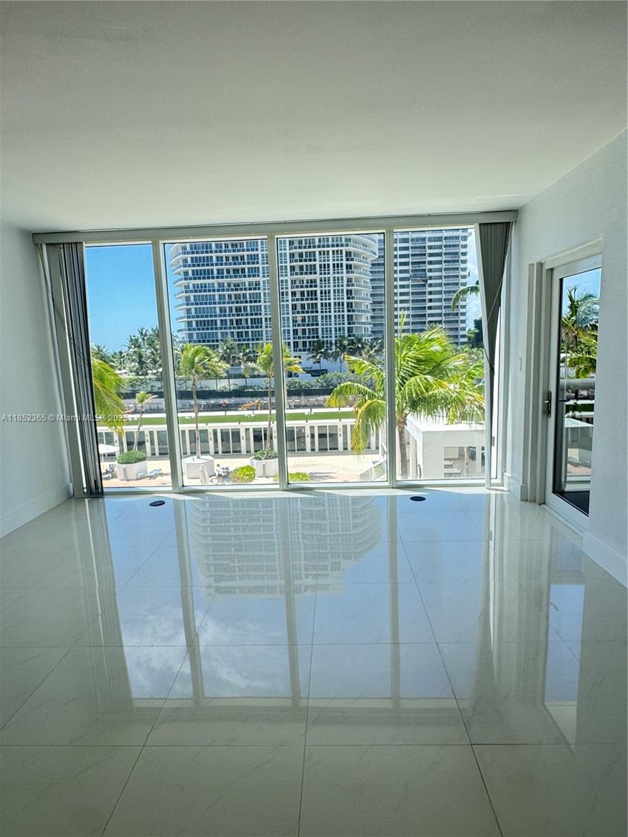 A bright, empty room with white tile floors features floor-to-ceiling windows overlooking a pool area — 10275 Collins Ave # 316, Bal Harbour FL 33154, BAL HARBOUR, FL