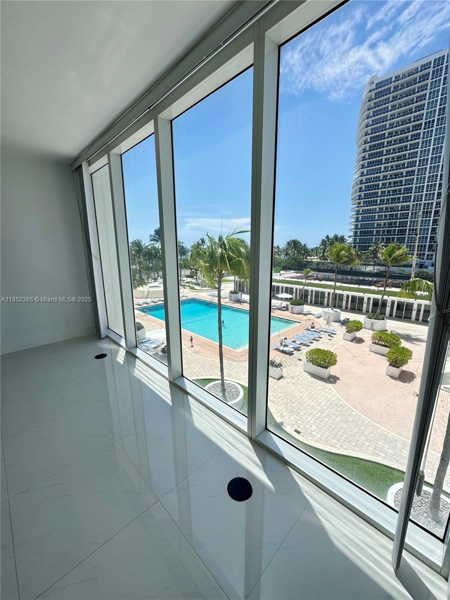 A bright room with floor-to-ceiling windows overlooks a swimming pool and a tall building — 10275 Collins Ave # 316, Bal Harbour FL 33154, BAL HARBOUR, FL