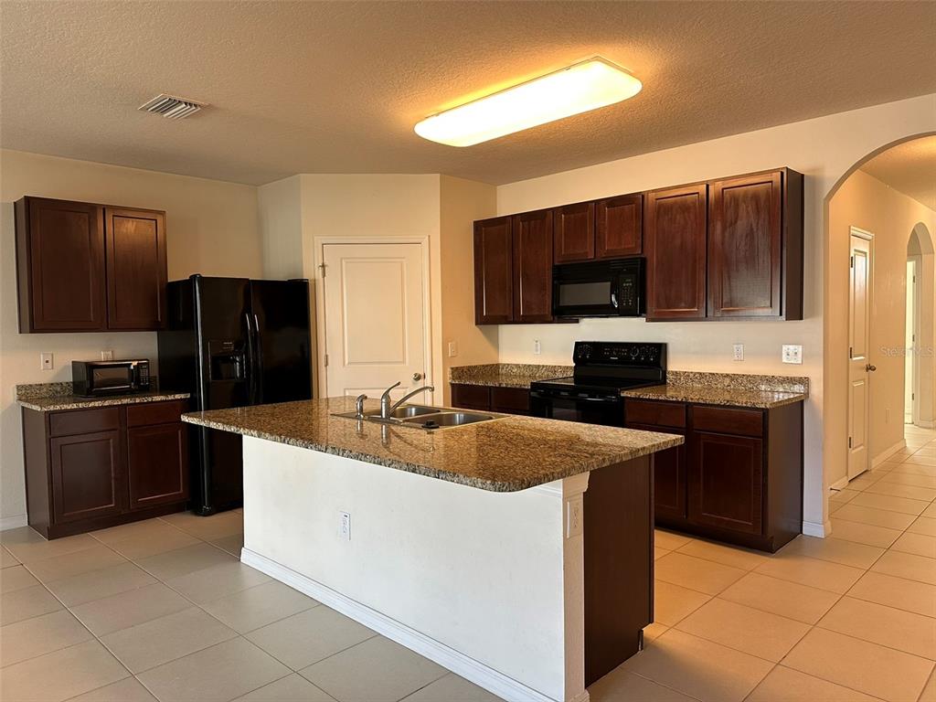 A kitchen features dark wood cabinets, granite countertops, a central island, and black appliances — 13515 HAVERHILL DRIVE, SPRING HILL, FL