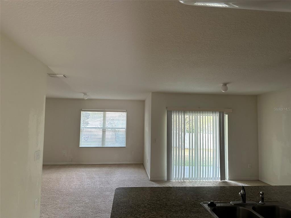 A carpeted living area with a window and sliding glass doors viewed from a kitchen — 13515 HAVERHILL DRIVE, SPRING HILL, FL