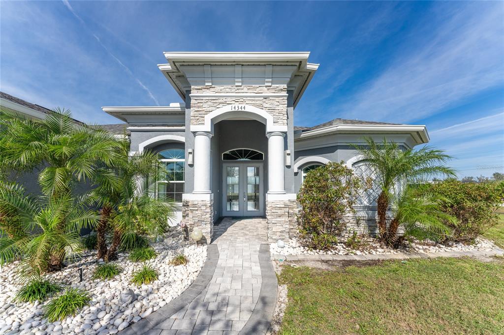 A single-story house exterior features a stone-accented entryway with white columns and double glass doors — 14344 AMESTOY AVENUE, PORT CHARLOTTE, FL