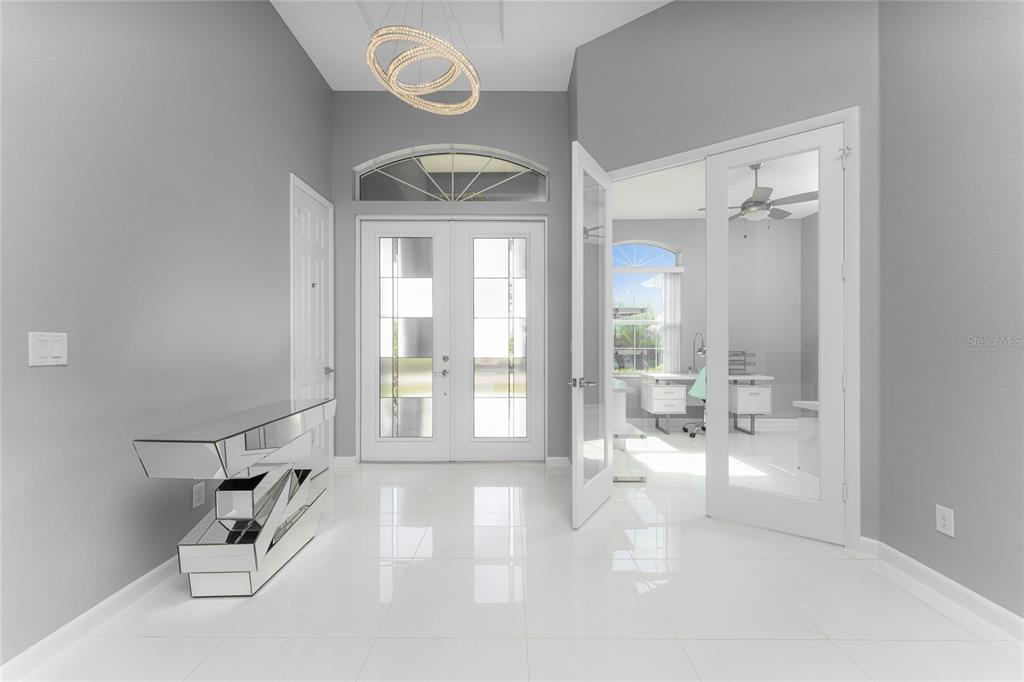 A bright foyer features white tile floors, a mirrored console table, and double glass doors — 14344 AMESTOY AVENUE, PORT CHARLOTTE, FL