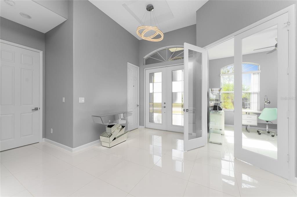 A bright entryway features white tile floors, grey walls, a mirrored console, and glass doors — 14344 AMESTOY AVENUE, PORT CHARLOTTE, FL
