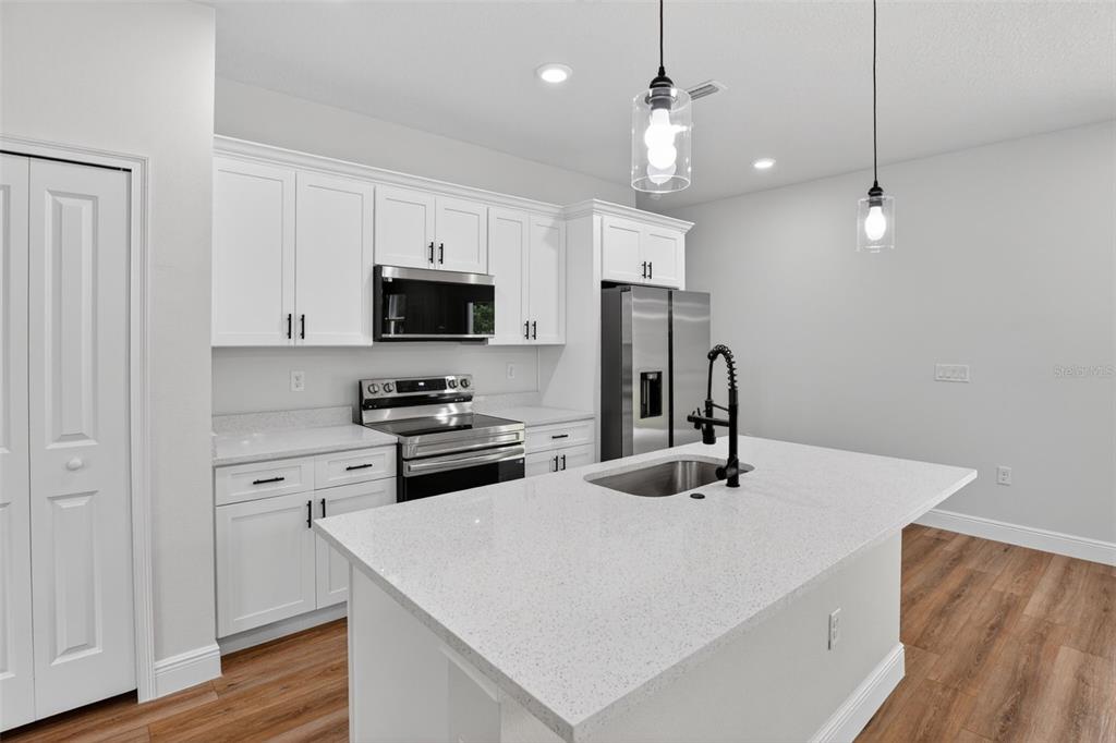 A modern kitchen features white cabinets, stainless steel appliances, a quartz island, and wood flooring — 8135 N TINY LILY DRIVE, CITRUS SPRINGS, FL