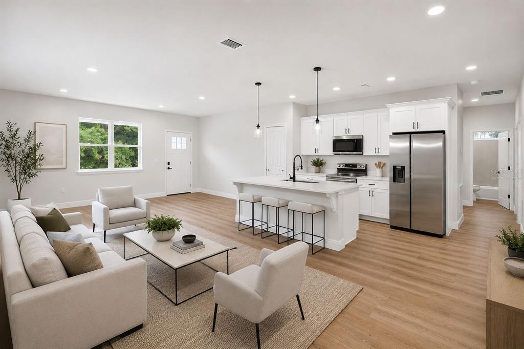 A bright open-concept living room and kitchen featuring white cabinetry, stainless appliances, and wood flooring — 8135 N TINY LILY DRIVE, CITRUS SPRINGS, FL
