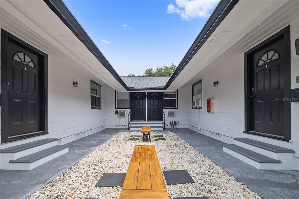 A courtyard with gravel, wooden benches, and four black doors leading into separate units — 917 30TH AVENUE N UNIT 1, ST PETERSBURG, FL