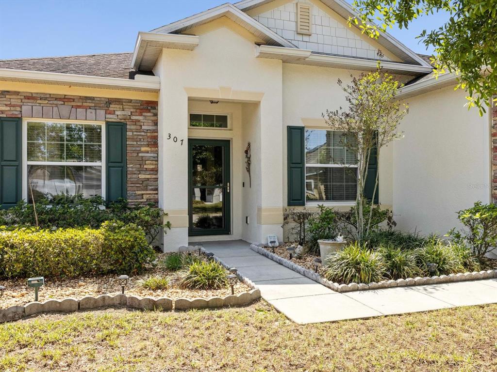A single-story house exterior features a stone facade, dark green shutters, and a covered entryway — 307 GLADESDALE STREET, HAINES CITY, FL